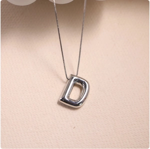 Detailed close-up of polished silver balloon letter D pendant necklace on a textured base