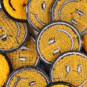 Stack of circular yellow smiley face embroidered patches with detailed needlework texture