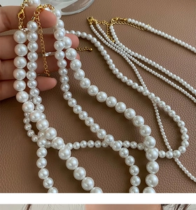 Détails de colliers de perles blanches superposés avec fermoirs dorés sur cuir