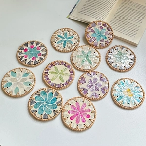 Macro detail of round rattan coasters with colorful shell flower inlay on white table