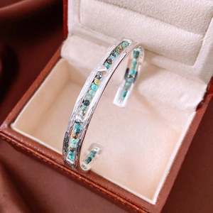 Macro shot of silver textured bangle inlaid with small turquoise stones on leather box