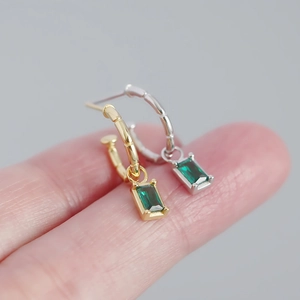 Macro shot of gold and silver C-shaped earrings with emerald zircon on fingertips