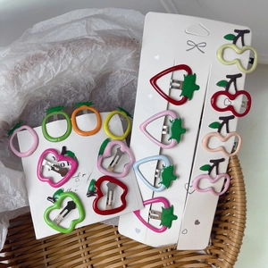 Detail view of colorful fruit-themed metal hair clips including strawberry and cherry shapes