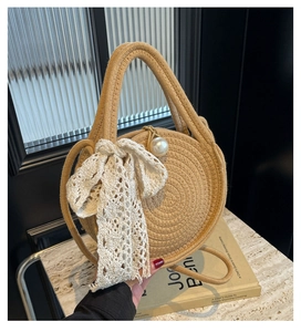 Detailed close-up of woven straw handbag with lace bow and large pearl charm
