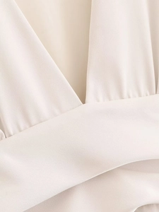 Detail eines eleganten cremefarbenen Satin-Kleides mit V-Ausschnitt und Taillenkreuzung