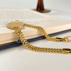 Detail of gold chain bracelet featuring coin pendant and blue evil eye charm on a book