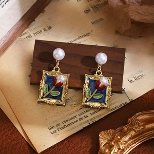 Detail of tulip enamel earrings with pearls, gold frames, and vintage French newspaper