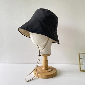 Close-up of black nylon bucket hat with beige lining and adjustable windproof strap