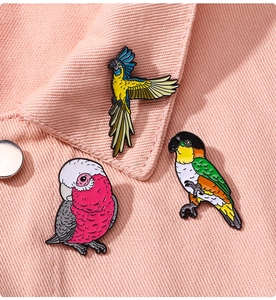 Detailed view of three colorful enamel parrot metal pins on pink denim fabric