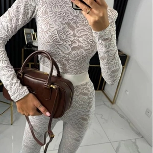 Detailed view of white lace long sleeve bodysuit with waist belt and leather handbag