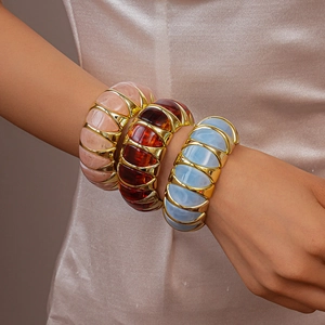 Detail of three chunky resin bangles in pink and amber with gold-toned metal link connectors
