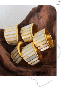 Macro shot of gold wide bands with white shell inlay stacked on natural wood texture