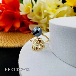 Detail of golden monstera leaf ring with black pearl on white display stand