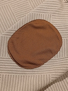 Detailed close-up of a beige knitted hoodie with contrast brown round elbow patches