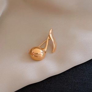 Macro view of a 14k gold plated musical note brooch on soft beige satin fabric