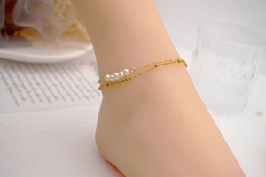 Detail of double-layer gold titanium steel anklet with five white pearls on model ankle