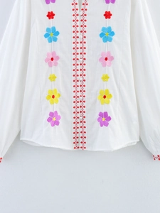 White long-sleeve blouse featuring colorful floral embroidery and geometric patterns