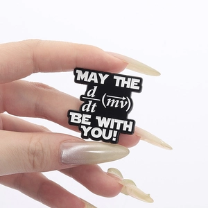Close-up of black enamel pin with physics formula engraving held by hand over white background