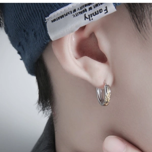 Detailed close-up of a silver-based hoop earring with golden flame textures on a male ear