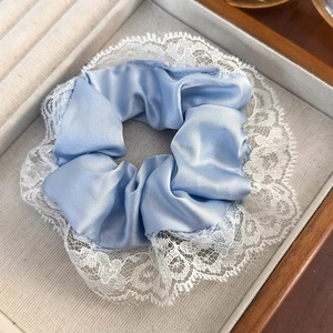Close-up of blue satin plaid scrunchie with delicate white lace trim on a beige tray