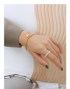 Detail of 18K gold-plated beaded bracelet with heart pendant and pearl ring on hand