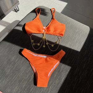 Detail of orange textured bikini top featuring golden chain straps and round metal charms