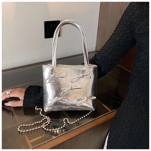 Close-up of silver metallic square handbag with 3D bow details and beaded chain strap