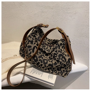 Close-up of leopard print canvas bag with brown leather strap and gold metal hardware