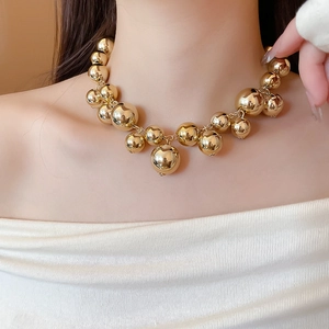Detail shot of a modern gold beaded necklace with high-polish metallic spheres on skin