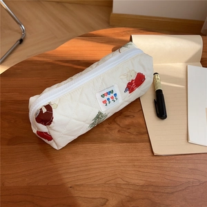 Close-up of quilted cream pencil case with bunny and tulip patterns on a wooden desk