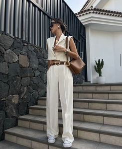 Outdoor shot of white sleeveless vest and wide-leg trousers set with brown leather bag