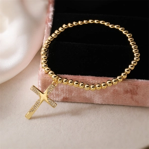 Detail of gold beaded bracelet with zircon-encrusted cross on pink velvet box