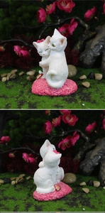 Close-up of white resin hugging cats figurine with pink roses on forest moss background