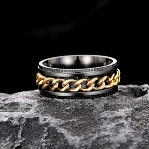 Macro shot of black spinner ring with golden Cuban chain inlay on dark rock surface