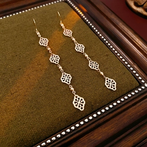 Macro detail of gold-plated geometric long earrings on a luxury green velvet background
