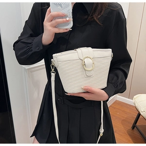 Detail of off-white woven bucket bag with gold metal buckle on a model in a black dress