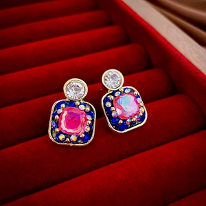 Close-up of vintage square earrings with pink and blue gemstones on red velvet