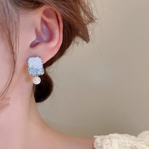 Close-up of geometric silver earring with blue resin inlay and elegant white pearl detail