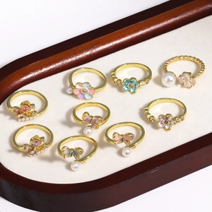 Set of 9 gold-plated open rings featuring butterfly, flower, and pearl designs on a display