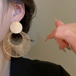 Close-up of model wearing large gold geometric round earrings with woven wire details