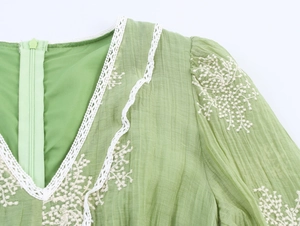 Macro detail of V-neckline featuring white lace trim and floral embroidery on green fabric