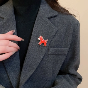 Detailed close-up of a red resin horse brooch with golden snowflake on a grey blazer lapel