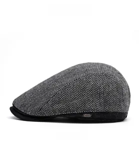 Dettaglio cappello newsboy in tweed a spina di pesce grigio con visiera nera e logo