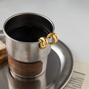 Close-up of gold stainless steel hoop earrings placed on a cup rim in a lifestyle setting