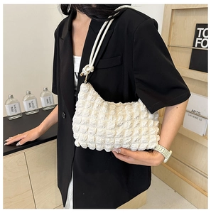 Detail of white pleated handbag with bubble texture and woven strap shown on model