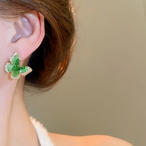 Detail of crystal butterfly earring with green stones and rhinestones worn on ear