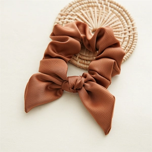 Detailed close-up of brown bow-knot scrunchie with soft fabric texture on rattan mat