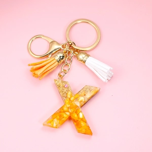 Detail of letter X resin keychain with gold foil flakes and colorful suede tassels