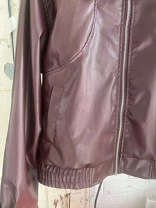 Detail of dark wine red faux leather jacket showing zipper pockets and elastic hem
