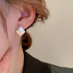 Boucles d'oreilles carrées nacrées avec bordure en métal doré brossé sur un modèle
